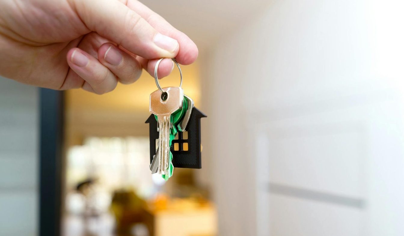 Eine Hand, die in einer modernen Wohnung Hausschlüssel hält, symbolisiert den Erwerb oder die Anmietung einer Immobilie.